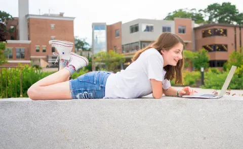 A UNE student works on her laptop outside the Danielle N. Ripich Commons